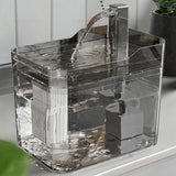 Clear acrylic water fountain on a reflective surface with a plant in the background